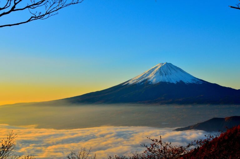Breathtaking view of Mount Fuji at sunrise, surrounded by misty clouds and vibrant sky.